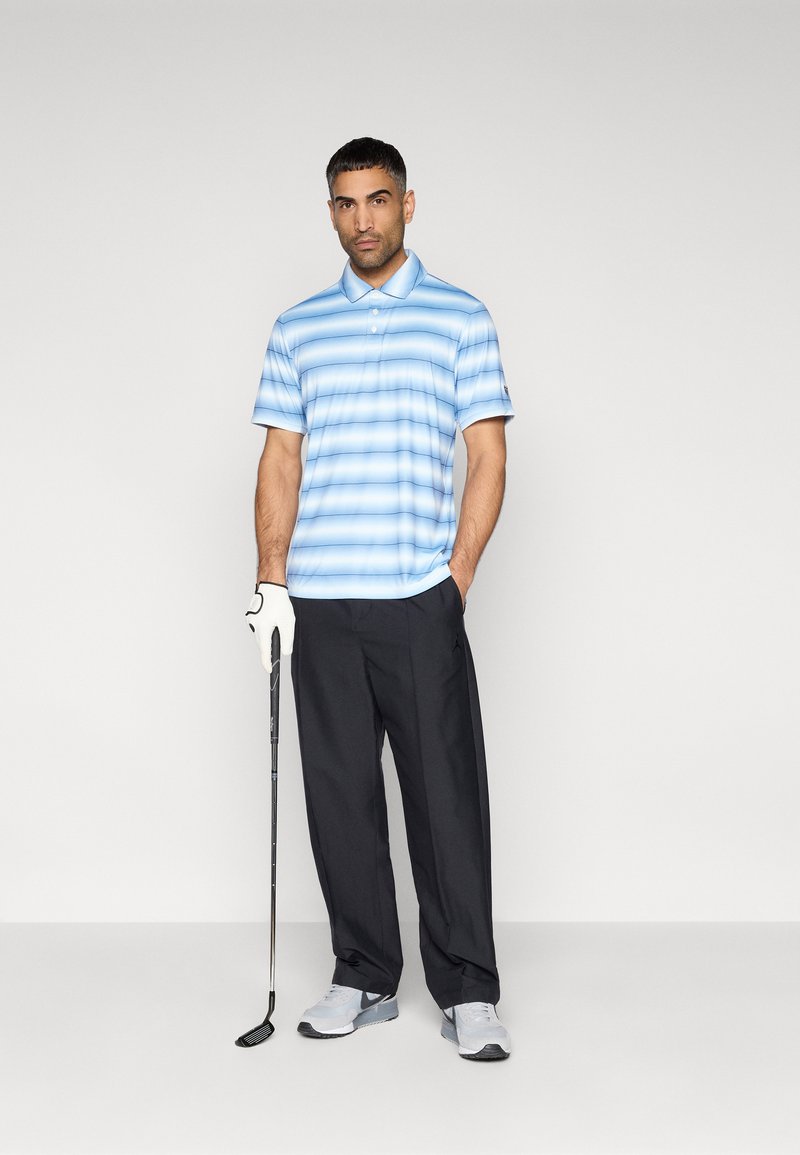 Golf-Outfit mit einem hellblau-weiß gestreiften Polohemd, schwarzer Hose, weißem Handschuh und grauen Sportschuhen, hält einen Golfschläger.