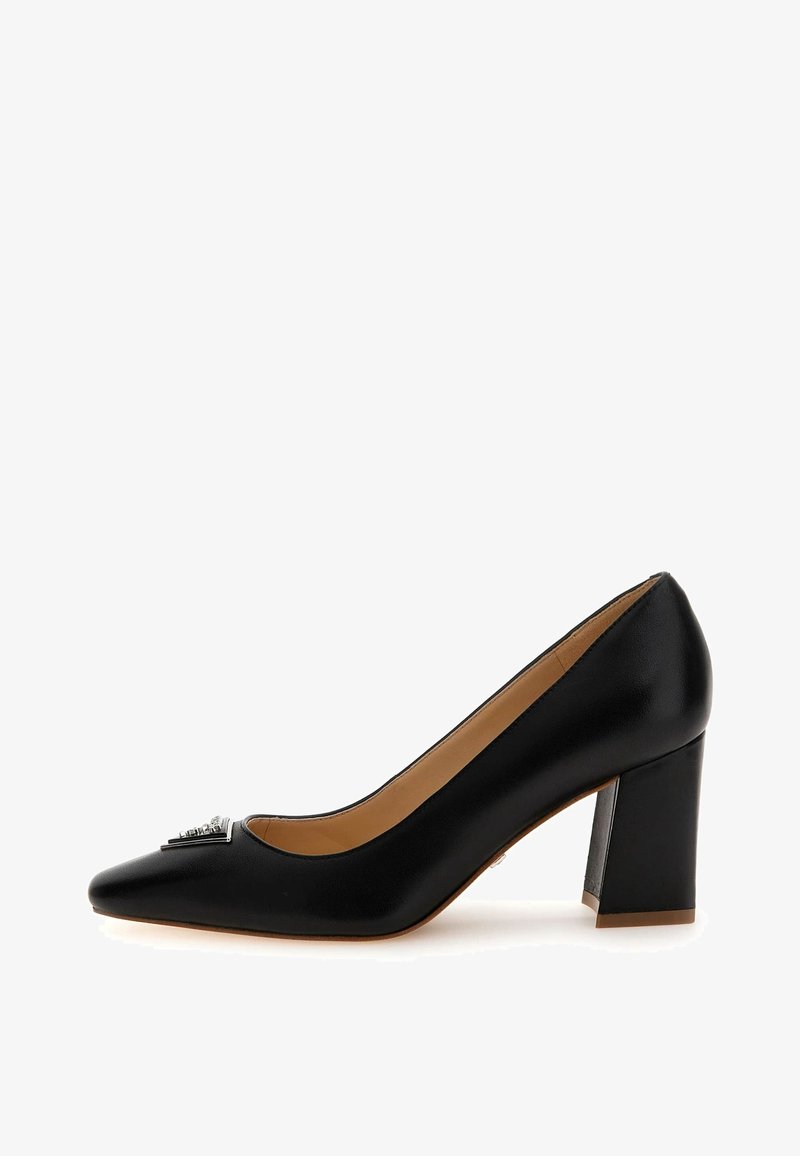 Escarpin en cuir noir à talon moyen, bout pointu avec un emblème décoratif argenté à l'avant, finition lisse et doublure intérieure beige.