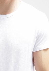 Hvid t-shirt med korte ærmer, rund halsudskæring og en let struktureret kvalitet, der viser en afslappet pasform og et enkelt design.