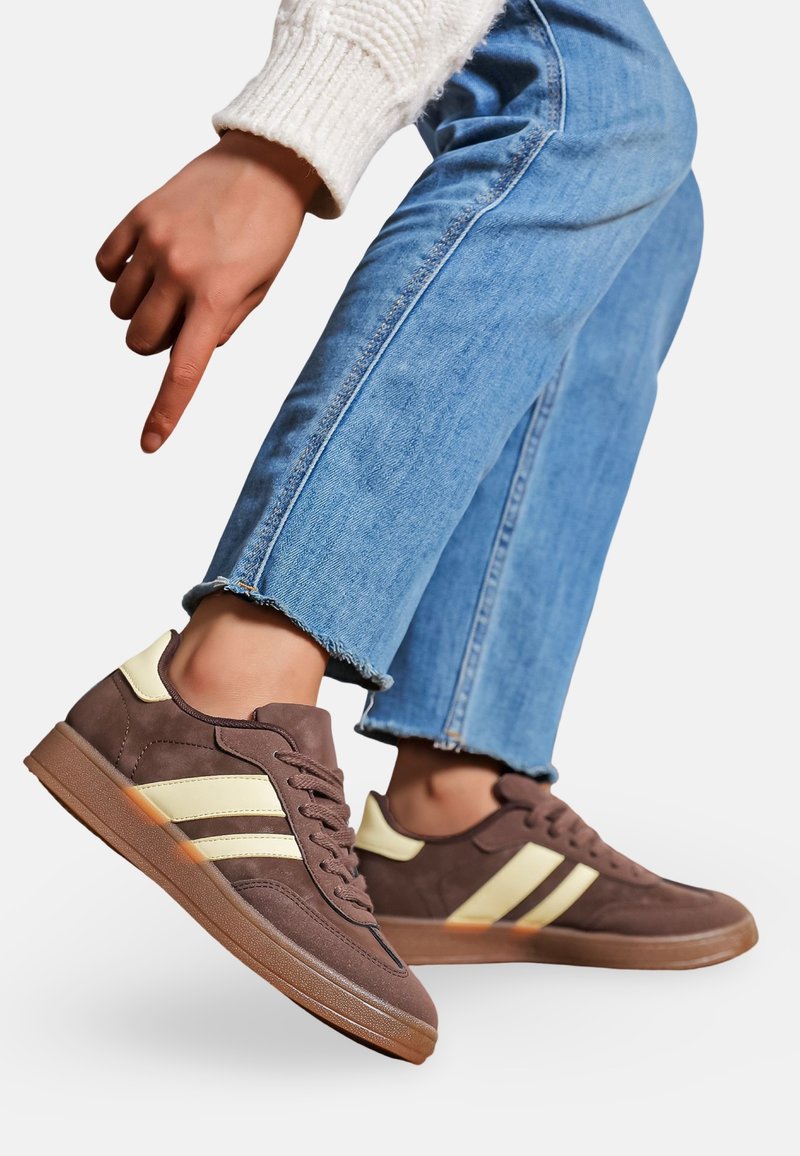 Baskets marron avec des rayures jaune clair, en daim et en caoutchouc, profil bas, design à lacets, semelle plate et accents texturés.