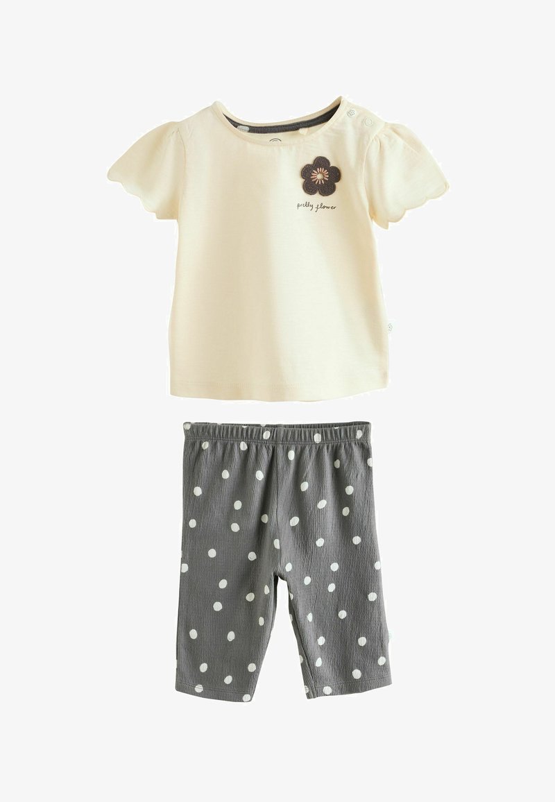 Chemise pour bébé à manches courtes crème avec bords festonnés et texte "jolie fleur", associée à des leggings gris à pois blancs.