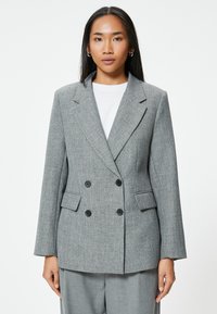Blazer gris de doble botonadura con patrón de pata de gallo, solapas con muesca y dos bolsillos frontales. La tela parece texturizada y estructurada.