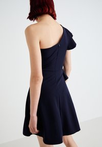 Vestido azul-marinho com um design assimétrico de um ombro, corpete justo e saia de corte evasê. Inclui um fecho oculto nas costas.