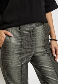 Pelēkās krokodilu raksta mākslīgā āda bikses ar gludu tekstūru, taisnas griezuma un sānu kabatām.