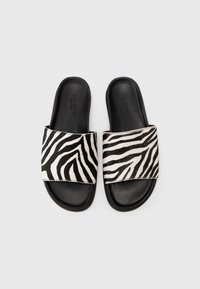 Slide-sandaler med en bred zebrarand i svart och vitt, kompletterat av en solid svart sula. Slät textur, minimal design.