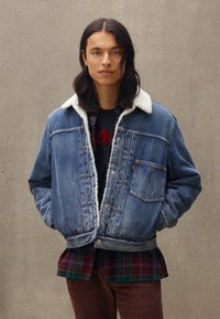 Denim jack met een sherpa-kraag, voorzien van een borstzak en een losse pasvorm. Gekocht over een geruite blouse en donkere broeken. Gestructureerde blauwe stof.