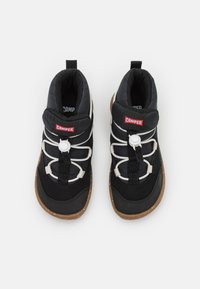 Zapatillas altas de tela negra con suela de goma, que cuentan con cordones elásticos blancos y una etiqueta de logo roja en la lengüeta y la parte trasera.