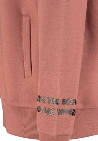 Rosa Sweatshirt mit weicher Textur, ausgestattet mit einer Kängurutasche und gerippten Bündchen. Der Text "LIKE YOU BECAUSE YOU ARE DIFFERENT" ist in Schwarz auf der Vorderseite aufgestickt.