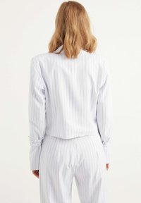 Vitt kostymjacka med lång ärm och kort design, tillsammans med matchande byxor. Har uppvikta ärmslut och en slät textur.