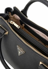 Sac à main Guess en cuir noir avec fermetures éclair dorées, double poignées, et doublure intérieure beige ornée du logo de la marque.