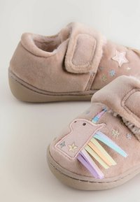 Chaussons doux en rose avec une texture pelucheuse, présentant un design de licorne et des accents en ruban coloré. Des étoiles brodées ajoutent des détails. Sangle réglable.