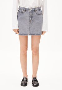 Jupe en denim avec un délavage bleu, design à cinq poches et coupe droite. Portée avec une chemise blanche à manches longues et des mocassins noirs.