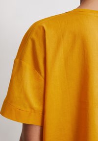 Geel linnen top met korte mouwen en een ronde halslijn in een relaxte pasvorm. Heeft zichtbare stiksels en een gladde textuur. Geen opvallende ontwerpelementen.