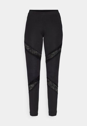 Leggings pretos com recortes triangulares adornados com renda preta nas laterais, feitos de um tecido elástico com um design ajustado.