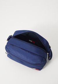 Borsa a tracolla blu navy realizzata in tessuto resistente, dotata di chiusura con zip, anello in metallo laterale e etichetta con logo sul davanti.