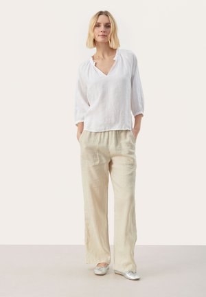 Witte linnen blouse met een V-hals en geschulpte kraag, gecombineerd met losse beige linnen broek. Zilveren ballerina's met strikdetails maken de look compleet.