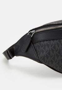 Sac banane en nylon noir avec des accents en cuir, doté d'une fermeture éclair en métal argenté, d'un motif de logo en relief et d'une sangle ajustable pour un ajustement varié.