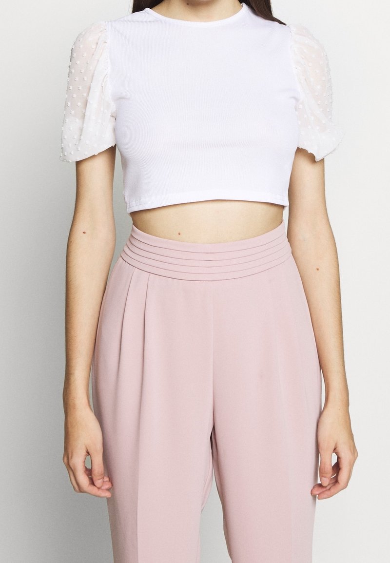 Bílý žebrovaný crop top s průhlednými volánkovými rukávy pokrytými puntíky, spárovaný s světle růžovými kalhotami s vysokým pasem a sklady.