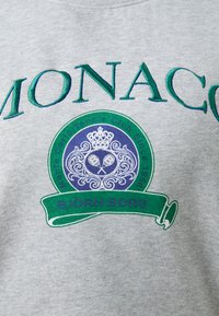 Šedá mikina s vyšívaným dizajnom v zelenej a modrej farbe s nápisom "MONACO", kruhovým logom, motívmi tenisových rakiet a "BJÖRN BORG."
