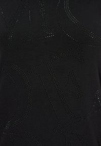 Musta t-paita, jossa on teksturoitu muotoilu ja rei'itetyt kirjaimet. Silkkinen kangas, jolla on hienovarainen kiilto, korostaen kirjainkuvioita.