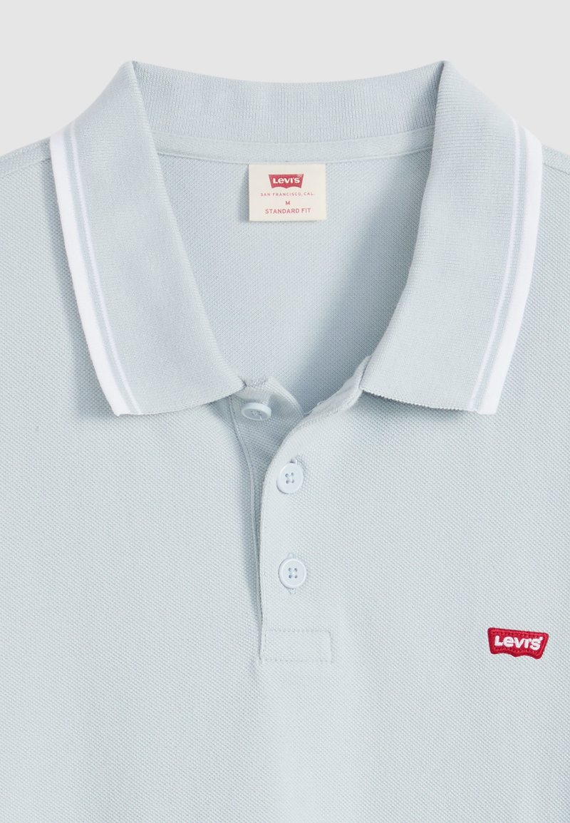 Polo Levi's de color azul claro con rayas blancas en el cuello, tres botones y un logo rojo de Levi's en el pecho. Corte estándar, talla mediana.