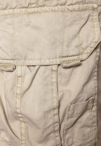 Shorts cargo beige in cotone morbido, caratterizzati da numerose tasche, cuciture in vista e una leggera texture stropicciata.