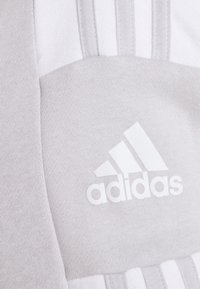 Tela atlética gris con un icónico logotipo blanco de Adidas y tres rayas blancas. La textura es suave e incluye detalles de punto fino.