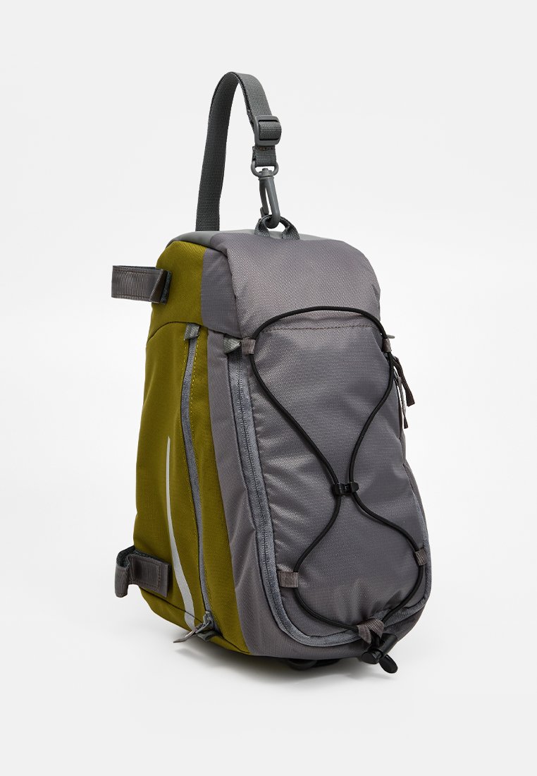 Zaino a tracolla grigio e verde oliva con corda elastica frontale, tasche con zip e tracolla regolabile, mostrato su uno sfondo bianco.