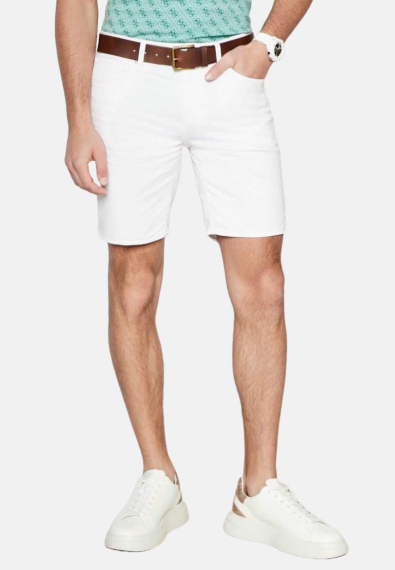 Pantaloni corti bianchi in cotone con una vestibilità dritta, abbinati a una cintura marrone e scarpe da ginnastica bianche. L'outfit presenta una camicia con motivo verde.