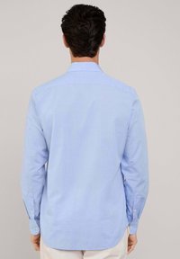 Camisa de manga larga azul claro con cuello abotonado, textura suave y dobladillo redondeado. Presenta botones en los puños y el yugo del hombro.