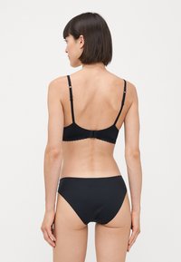 Schwarzes Lingerie-Set mit einer BH mit gewelltem Spitzensaum und passendem Bikini-Unterteil. Glatte Textur, verstellbare Träger und ein einfaches Design.