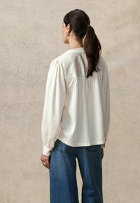 Crème-kleurige blouse met een gerimpelde kraag, opbollende lange mouwen en knoopmanchetten, gecombineerd met loszittende blauwe denim jeans.