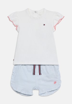 Camicia bianca a maniche corte con bordo rosso e logo abbinata a pantaloncini a righe blu e bianche con bordi arricciati e iniziali ricamate rosse.