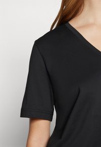 T-shirt nera a maniche corte con scollatura a V, realizzata in tessuto liscio, con una forma aderente e cuciture discrete lungo le maniche e il colletto.