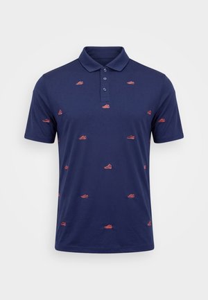 Laivastonsininen lyhythihainen poolopaita, jossa on kolme nappia ja pieniä punaisia tennarikuvioita kirjottuna kankaalle.