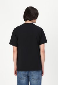 Zwarte katoenen T-shirt met korte mouwen, een ronde halslijn en een relaxte pasvorm, gedragen met blauwe jeans, gezien van achteren.