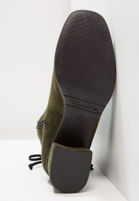 Botín de ante verde oliva con suela de goma negra texturizada. Detalle de cremallera lateral y cordones visibles, que ofrecen un ajuste seguro.