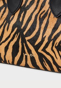 Svart og brun zebra-mønstret håndveske med en teksturert overflate, lærdetaljer og et gulllogo.