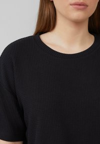 Zwart, textuur kortemouwen top met een ronde halslijn en een subtiel wafelpatroon. Het materiaal lijkt zacht en ademend.