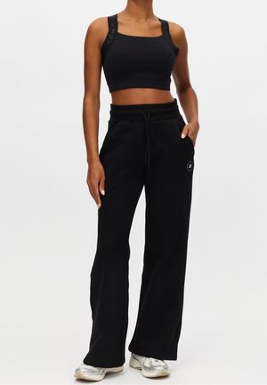 Vrouw draagt een zwart cropped athletisch tanktop en zwarte wijde joggingbroek met zakken, gecombineerd met witte en zilveren sneakers.