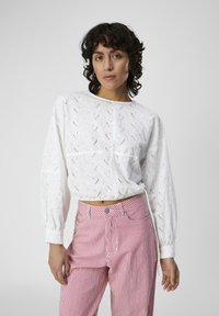 Blouse blanche en broderie anglaise avec de longues manches bouffantes et un col rond, associée à un pantalon rayé rose et blanc avec un bouton de fermeture à l'avant.