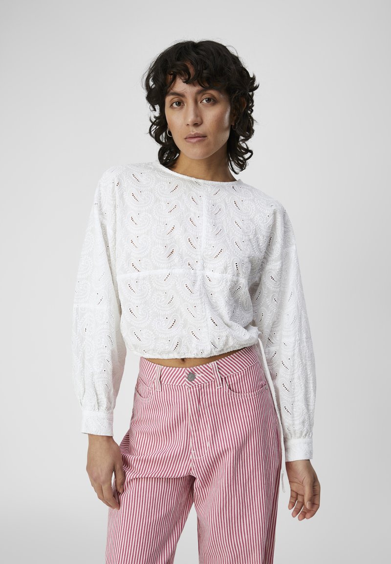 Blouse blanche en broderie anglaise avec de longues manches bouffantes et un col rond, associée à un pantalon rayé rose et blanc avec un bouton de fermeture à l'avant.