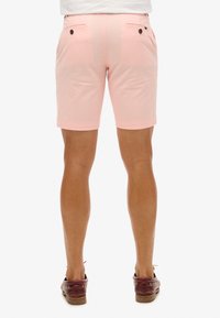 Shorts rosa de algodón, con bolsillos traseros con cierres de botón y dobladillo vuelto. Cintura visible y corte relajado.