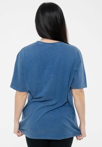 Blue cotton oversized t-shirt with short sleeves, round neckline, and a relaxed fit. Fabric appears slightly textured with a faded finish.