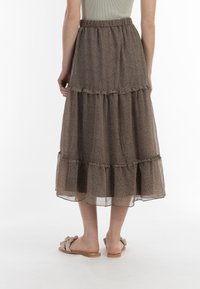 Brun, lagdelt maxi-nederdel lavet af letvægtsstof, der har en bølget kant og et lille blomstermønster, samt en elastisk talje for komfort.