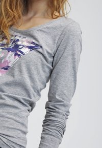 Maglia grigia a maniche lunghe con scollo a barca, caratterizzata da un design grafico colorato sul davanti in tonalità di viola e rosa.