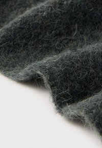 Mørkegrønt tekstureret stof med bløde, dunede fibre med en let glans og naturlig krølle, draperet ved kanten.