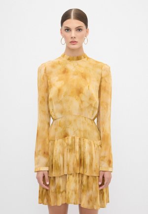 Vestido amarillo con un dobladillo con volantes y mangas largas, que presenta un cuello alto y una tela texturizada, semitransparente, con un patrón veteado.