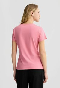 Kurzärmliges, rosa Baumwoll-T-Shirt mit Rundhalsausschnitt, glatter Textur und lässiger Passform, kombiniert mit schwarzen Hosen.