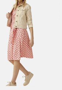 Chaqueta de mezclilla beige sobre un vestido rosa con un patrón geométrico, con una cintura atada y combinado con zapatillas ligeras.